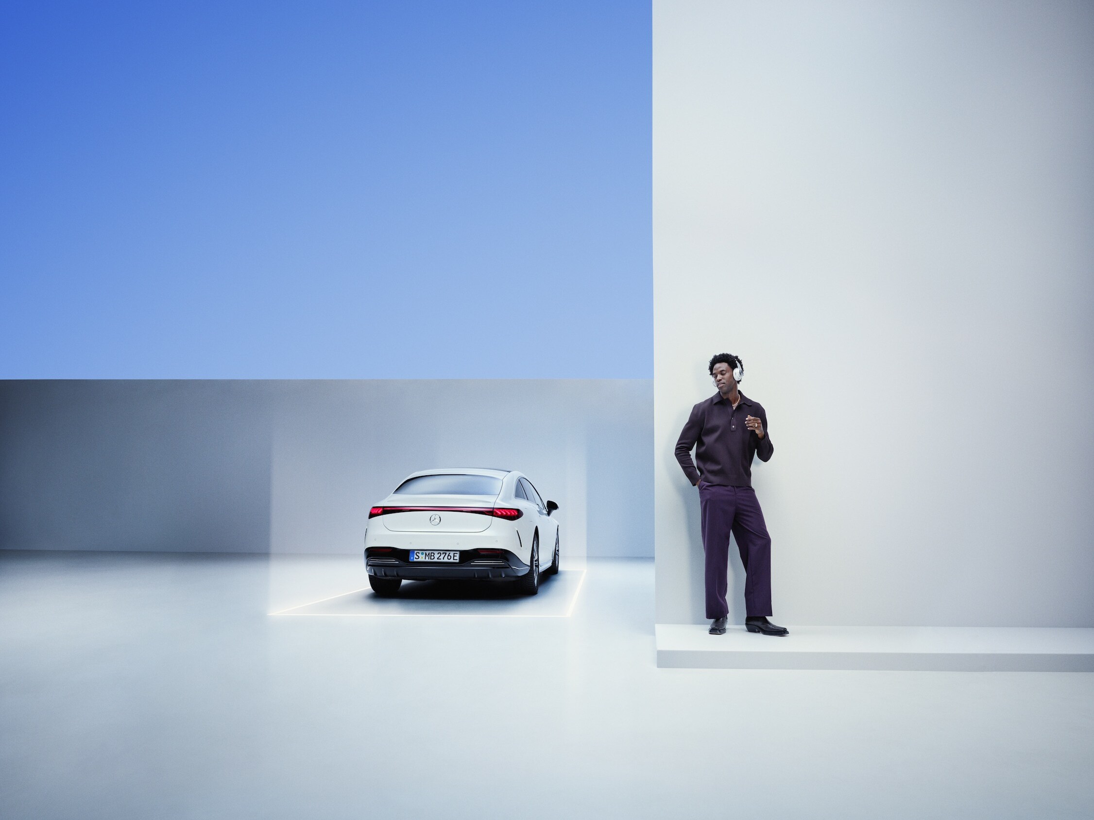 A man leans against a wall next to a Mercedes-Benz.